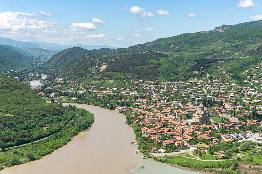 23 Amazing UNESCO Sites in Europe, Off the Beaten Track 5 Mtskheta in Georgia - a long winding river with a town on the right hand side and green hills beyond