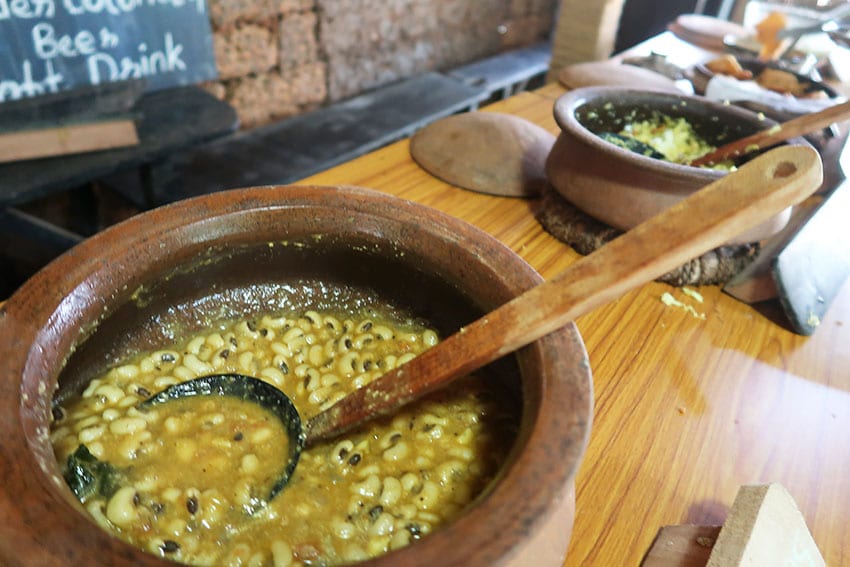 A Fascinating Tour around Tanshikar Spice Farm, South Goa 5 round clay pots with bean curry in with wooden ladle sitting on a wood bench other pots in the background at Tanshikar Spice Farm