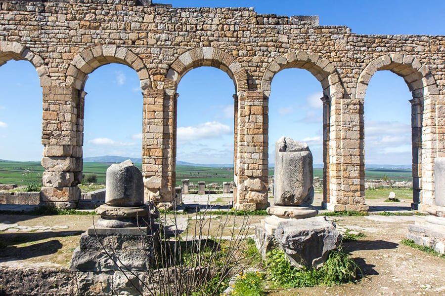 12 Amazing Unesco Heritage Sites In Africa - Off The Beaten Track 7 five arches made of sand coloured brick with a view of distant green fields and hills in the background and ruined pillars in the foreground