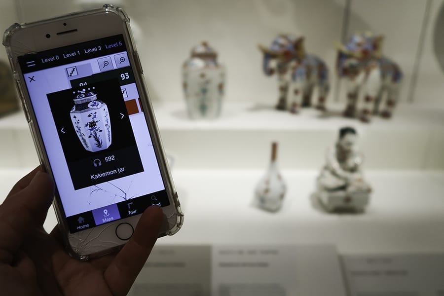 Mobile phone screen showing a vase with actual pottery vase, elephants and figurines in the background