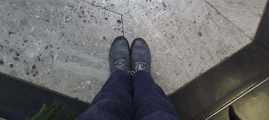 shot looking down on a pair of blue lace-up boots and jeans standing on a stone floor