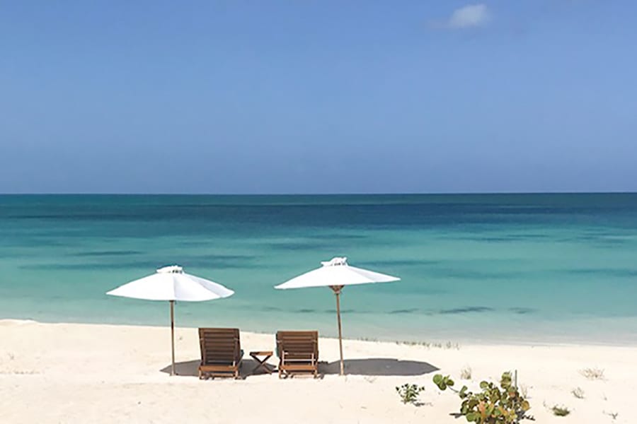 view of the sea from Barbuda with two sunbeds and white sunshades