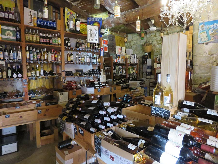 The inside of La Cave de Fayence with rows of bottles of wine on shelves and on tables. Red white and rose wine bottles