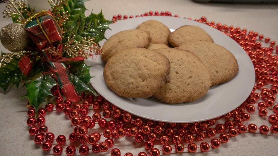 Favourite Christmas Bakes to try this year 5 white plate with round biscuits surrounded by red shiny beads and holly with a tartan bow.