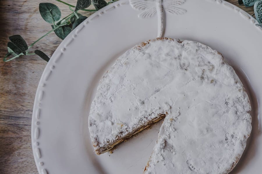 Favourite Christmas Bakes to try this year 9 round cake topped with icing sugar sitting on a round white plate with raised dragonfly motif. In the background is some ivy.