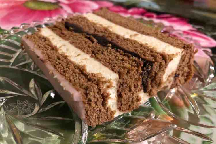 Favourite Christmas Bakes to try this year 6 A glass plate with piernik - a polish gingerbread - on it with layers of semolina custard, gingerbread and pink frosting on top