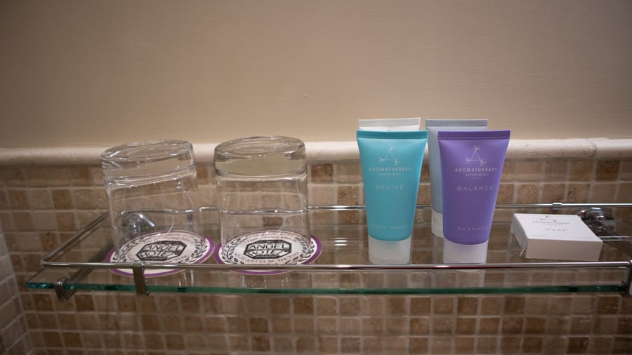 Glass shelf with two glasses and a turquoise, purple, white and blue tubes of Aromatherapy Associates