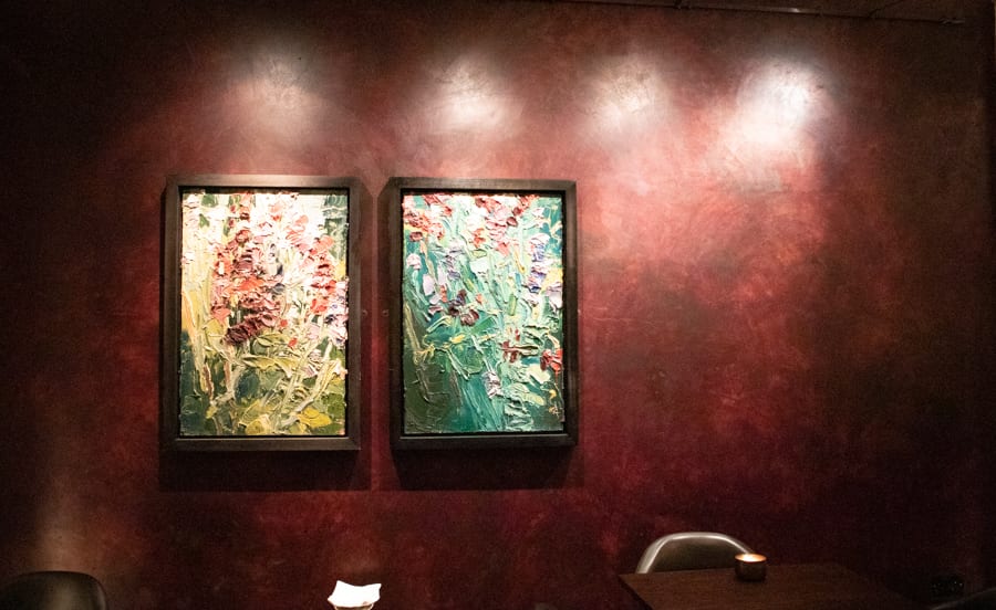 Two colourful Abstract paintings on a ruby red wall highlighted from above