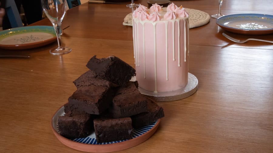 Artisan Bread Baking at the Abergavenny Baker 13 plate piled high with chocolate brownies next to a tall pale pink column cake with white chocolate drips down the sides and pink swirls on top