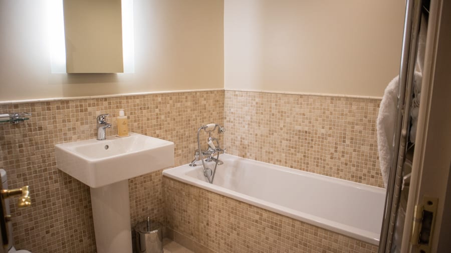 White bath and sink with small square tiles in colours of cream in The Angel Hotel Abergavenny