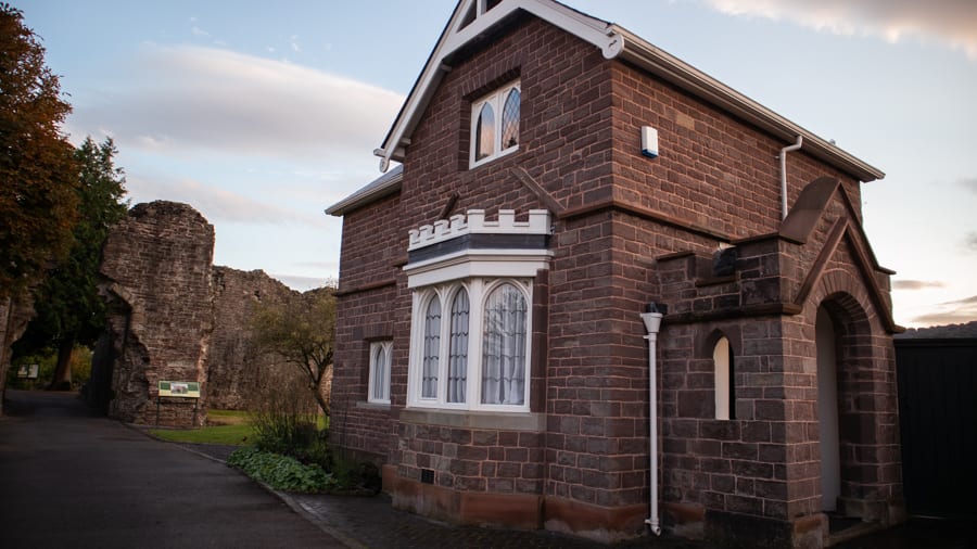 a brick built houses with a downstairs bay window with crenelations above and arched windows above. In the background you can see the ruins of Abergavenny Castle