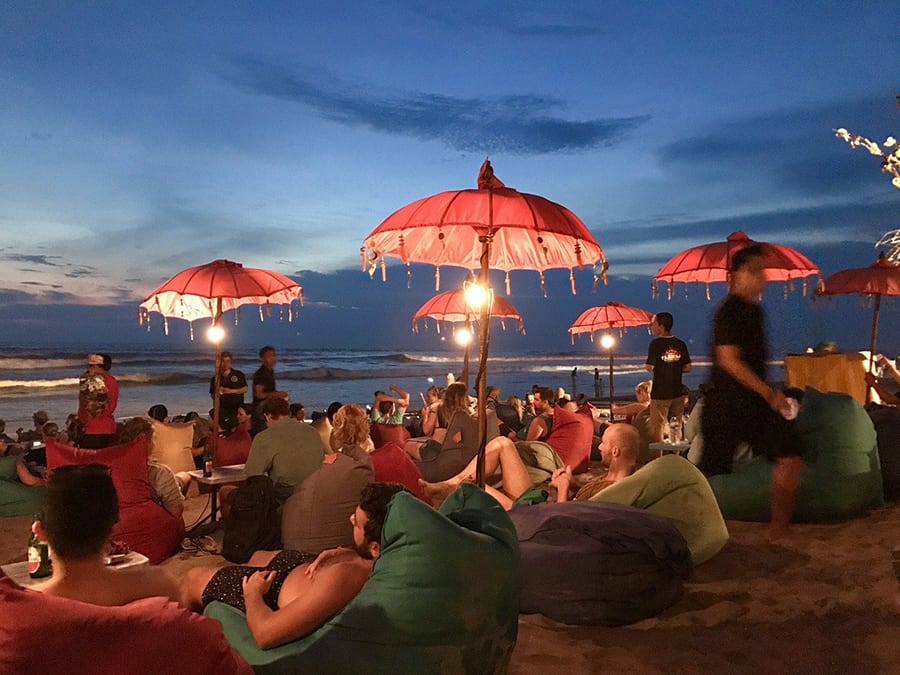 10 Great Reasons To Visit Indonesia 2 people relaxing on beanbags on Seminyak beach in the evening under red umbrellas
