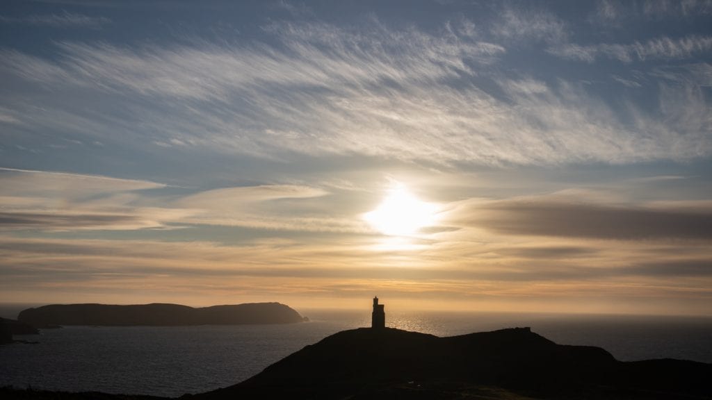 20+ Of The Best Things To Do In Port Erin, Isle Of Man (2023) 11 silhouette of a tower on at hill overlooking the sea with the setting sun and clouds in the sky