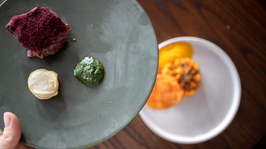 Versa - Responsibly Sourced Dining On The Isle Of Man 13 Beef with beetroot powder, wild garlic and potato stack on a gry plate with white plate below with carrot lattice, carrot puree