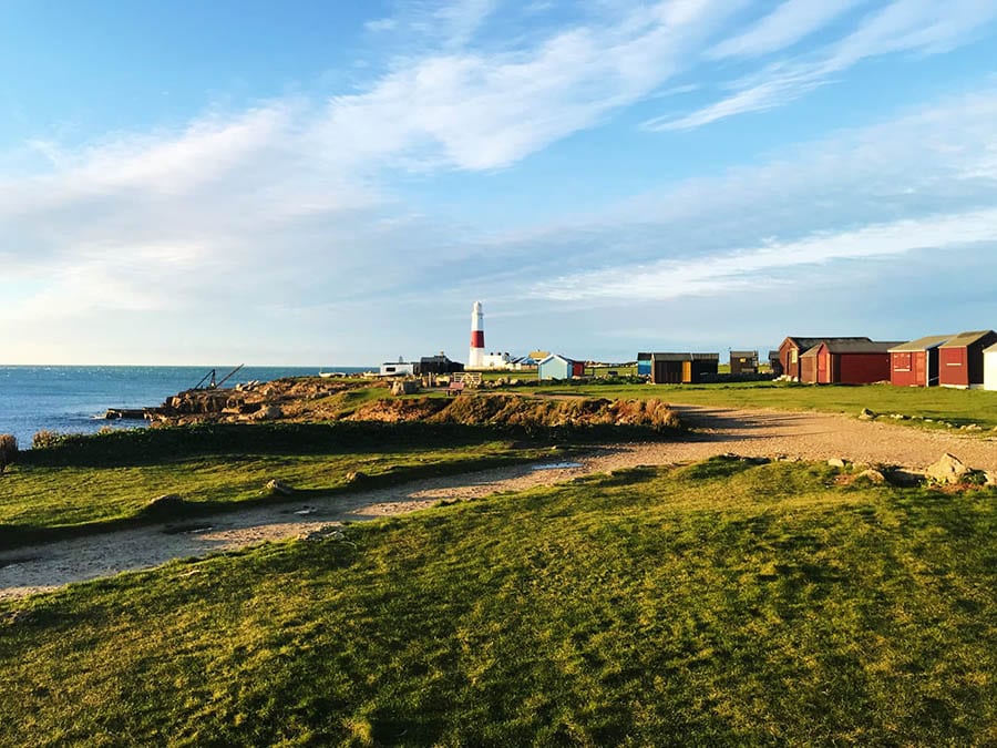 10+ Of The Best Weekends In Dorset 9 image looking over grass towards the lighthouse at Portland Bill with sea on the left and buildings on the right