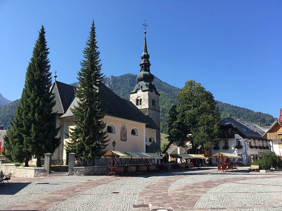 35+ Amazing Hidden Gems In Europe You Must Visit 24 blue skies above a church in Kranjska Gora with cobbled street in front