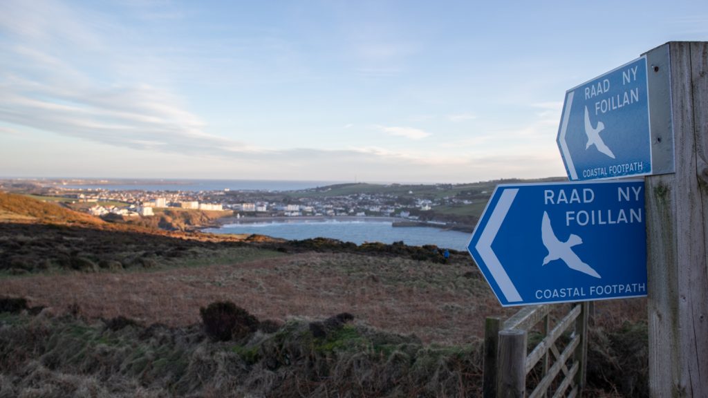 15+ Of The Best Things To Do On The Isle Of Man 15 two blue signs saying Raad Ny Foillan with a bay in the background