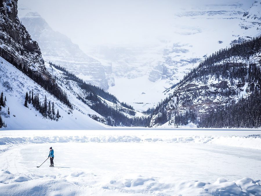 Banff - frozen lake with pine trees an a skater on the ice