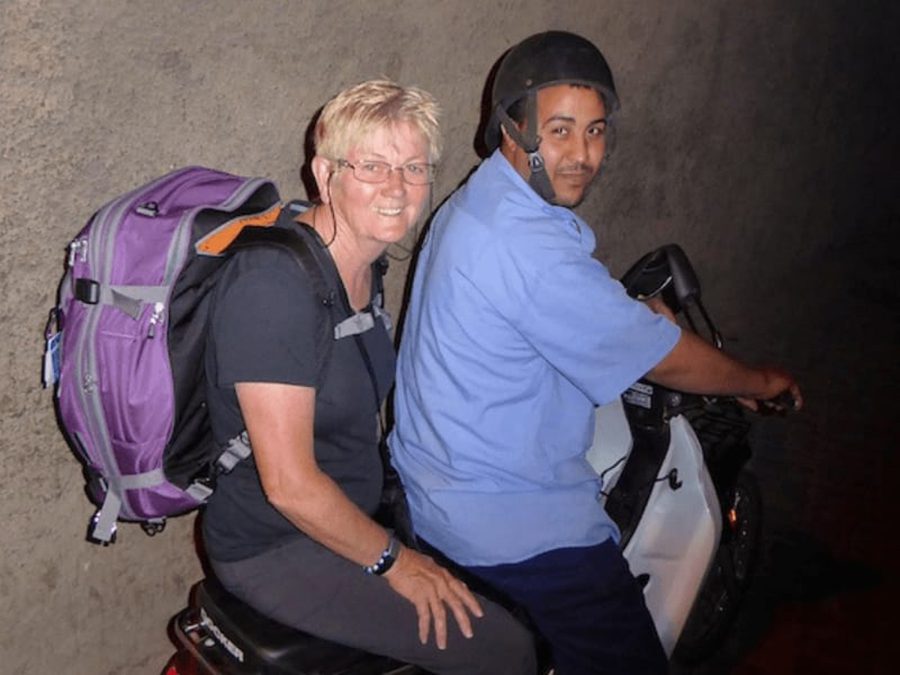 Celebrating 16 Awesome Mature Bloggers In 2021 To Inspire You 15 Anne from Packing Light Travel on the back of a scooter with her purple backpack on her back, one of the Mature bloggers