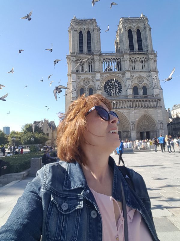 Celebrating 16 Awesome Mature Bloggers In 2021 To Inspire You 16 Susan from GenXTraveler with a cathedral behind her an pigeons flying around