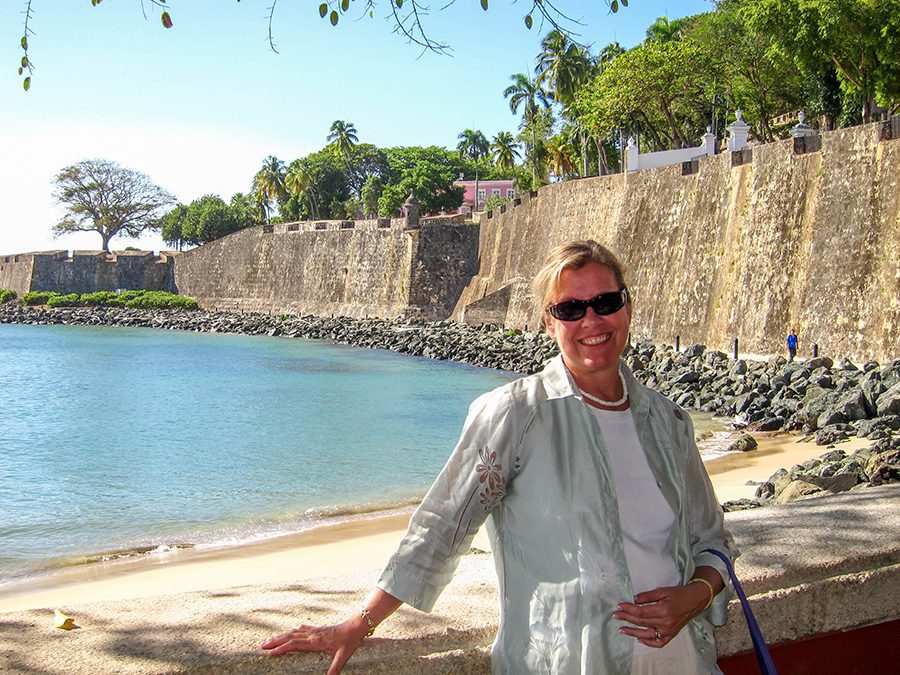 Celebrating 16 Awesome Mature Bloggers In 2021 To Inspire You 9 Amy from The Travelling Tulls' in Puerto Rico leaning against a wall with the sea behind her