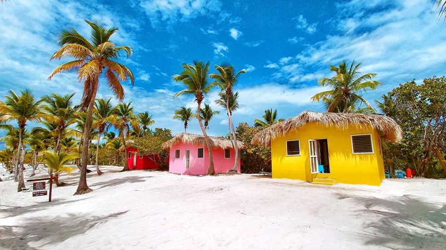 25 Amazing Destinations For Winter Sun Around The World 11 brightly painted beach shacks in yellow, pink and red surrounded by palm trees on white sand