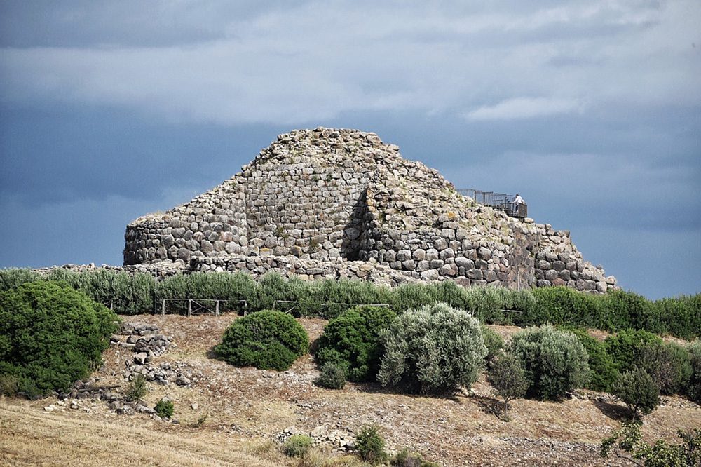 Stunning UNESCO Sites in Italy to discover in 2023 14 grey stone round semi-derelict structure with dark green scrub bushes in front