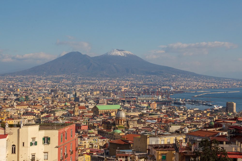 Stunning UNESCO Sites in Italy to discover in 2023 8 the town of Naples with the snow-capped Mount Vesuvius volcano in the background
