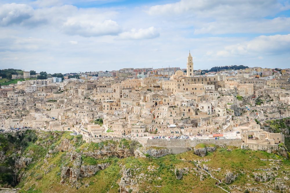 Stunning UNESCO Sites in Italy to discover in 2023 7 the cream coloured walled city of Matera with church tower prominent. The city is on a hill and the crags are below