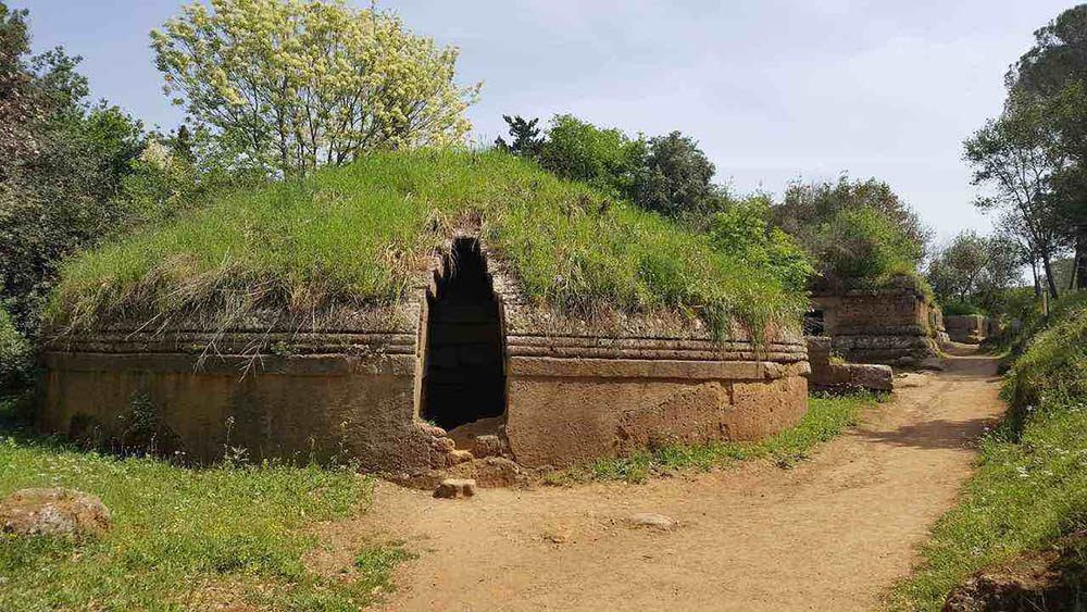 Stunning UNESCO Sites in Italy to discover in 2023 20 round grass roofed Etruscan Necropolis with opening cut into it and three bands around the middle of the round