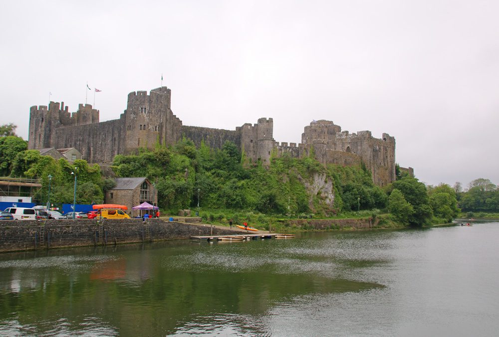 Pembroke Castle with a river in front of it and yellow kayaks to the left