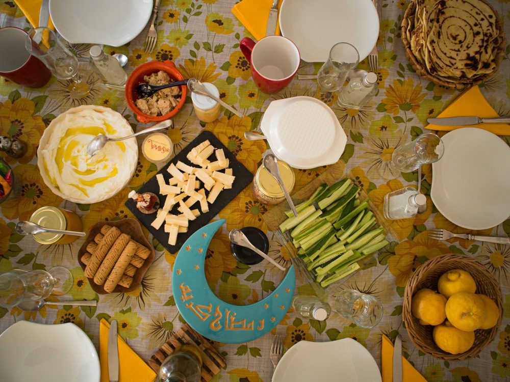 Sawa Taste of Tunisia: Explore the amazing food of Tunisia (2024) 45 Breakfast table with cut cucumbers, mwali, labneh, halva, a tuquoise crescent moon box with arabic writing on it, white plates, glassed and cups