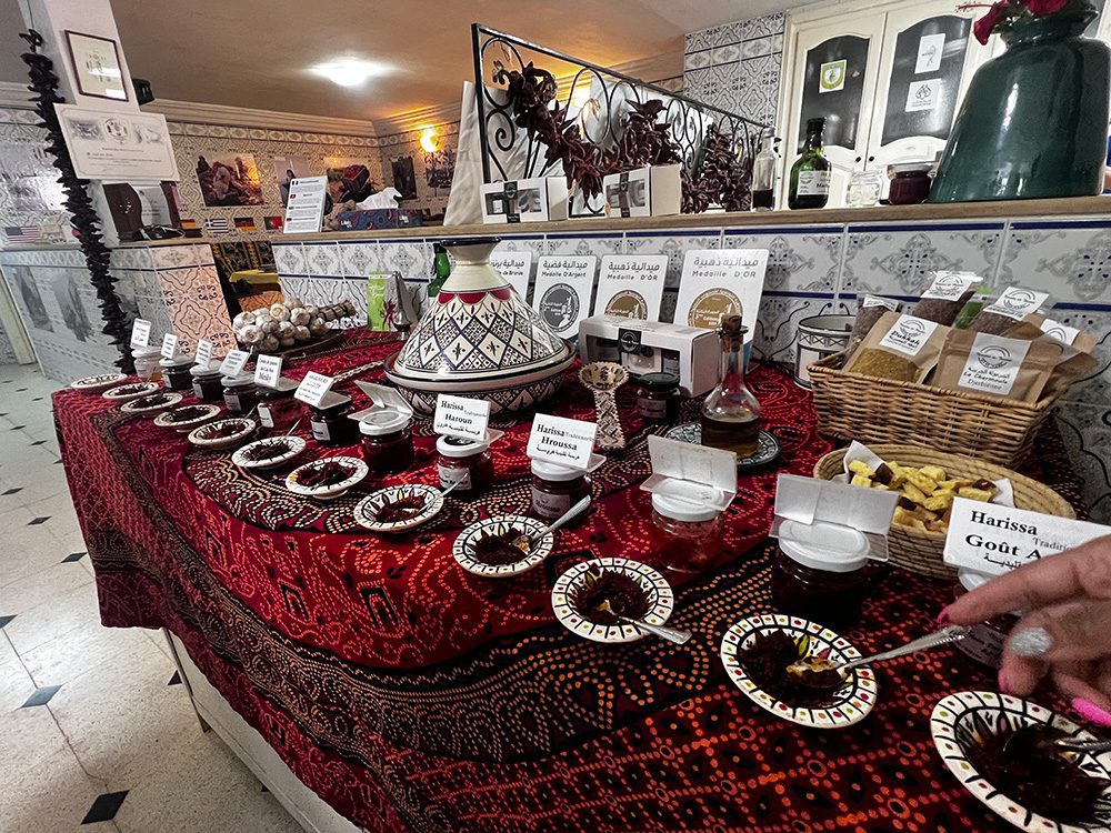 Sawa Taste of Tunisia: Explore the amazing food of Tunisia (2024) 9 selection of harissas in black and white small dishes with a large tagine behind them
