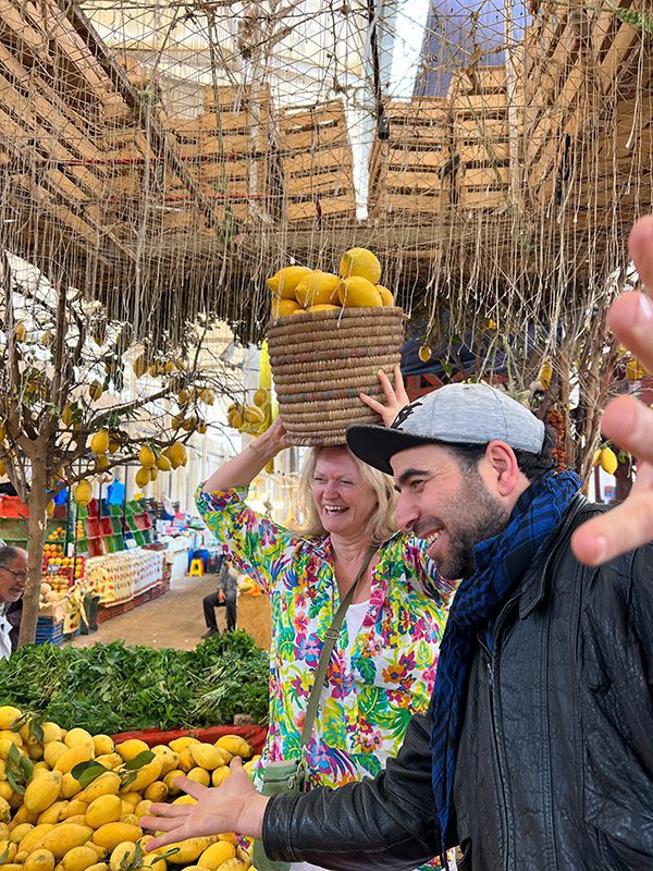 Sawa Taste of Tunisia: Explore the amazing food of Tunisia (2024) 21 holding a basket of lemons on my head beside Hamza in the Central Market with lemons around me.