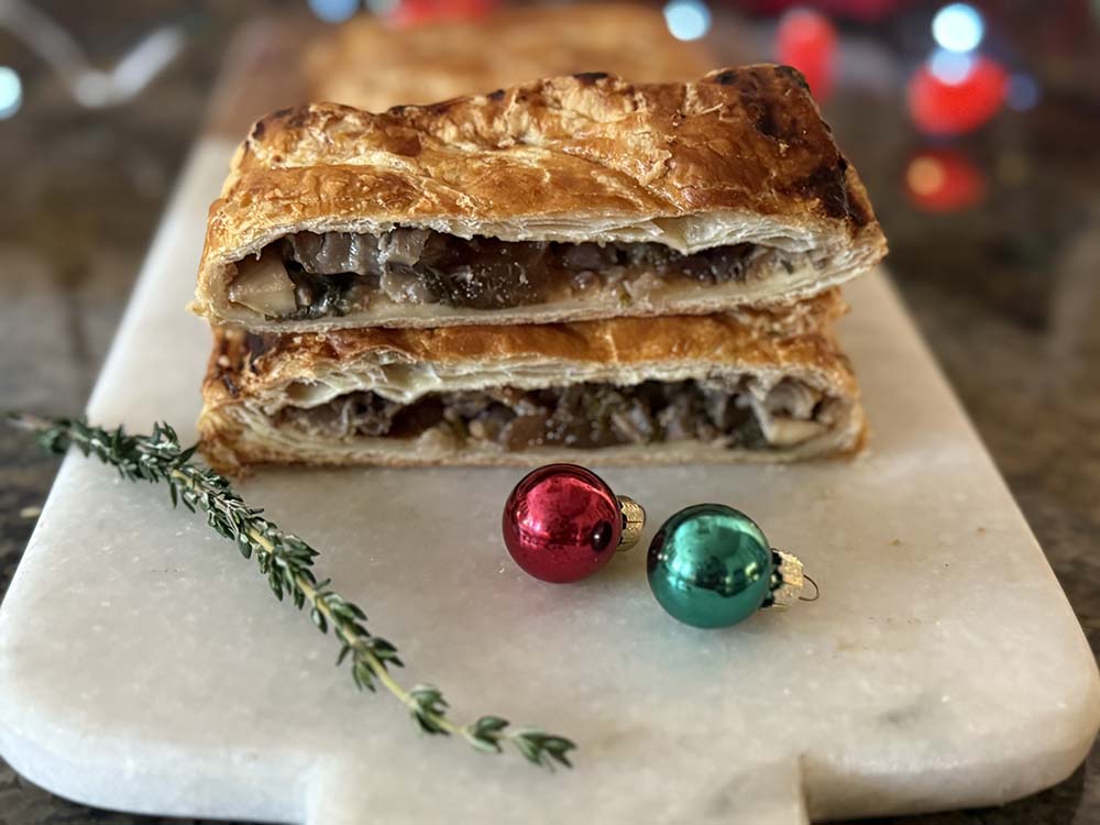 Mushroom Wellington with puff pastry and a green and red bauble and thyme sprig on a white board