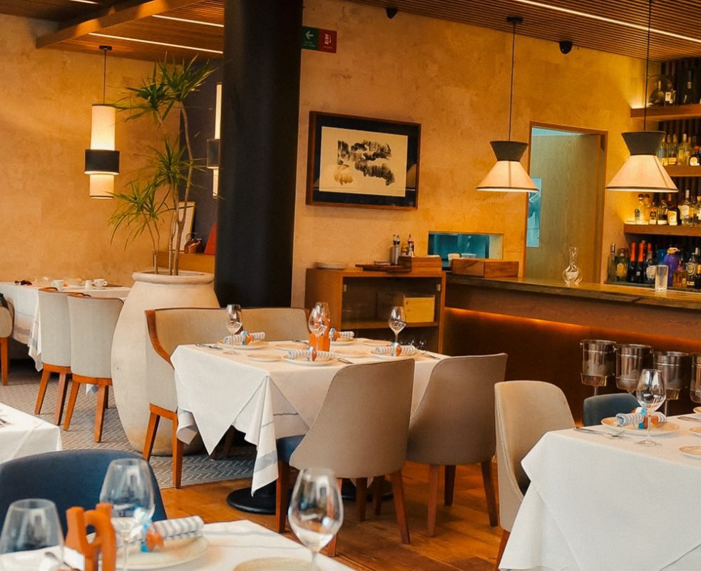 Zeru restaurant with tables with white linen table cloths, set with wine glasses, plates, cultery and pale blue and white striped napkins